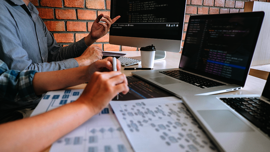 Zwei Personen vor Bildschirmen mit Source Code