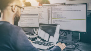 Man sits in front of screens showing source code