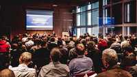 Großes Publikum sieht während einer Veranstaltung auf eine Leinwand