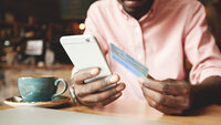 Man sitting in a cafe holding smartphone and ID card in his hands
